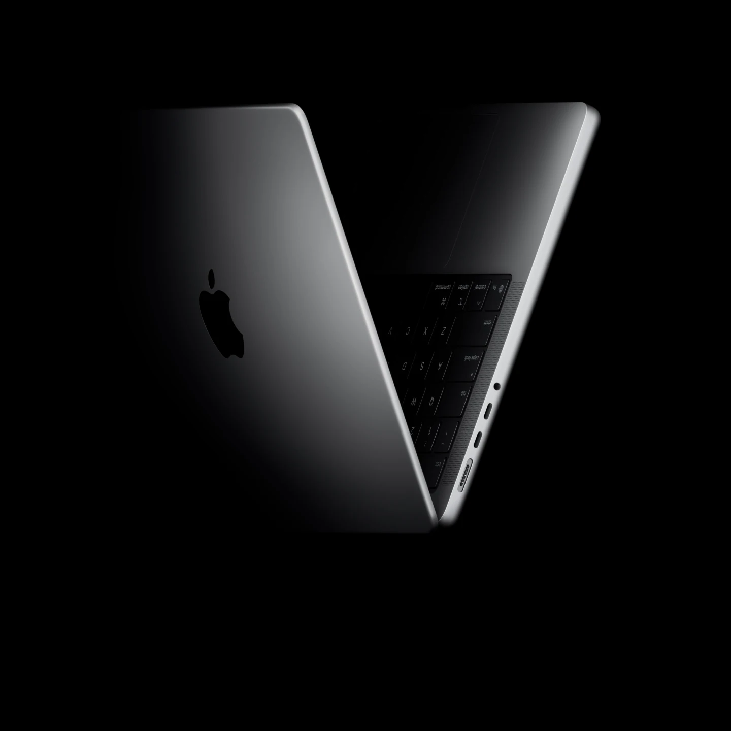 The MacBook Pro is shown from a rear three-quarter angle, highlighting its thin profile and ports.