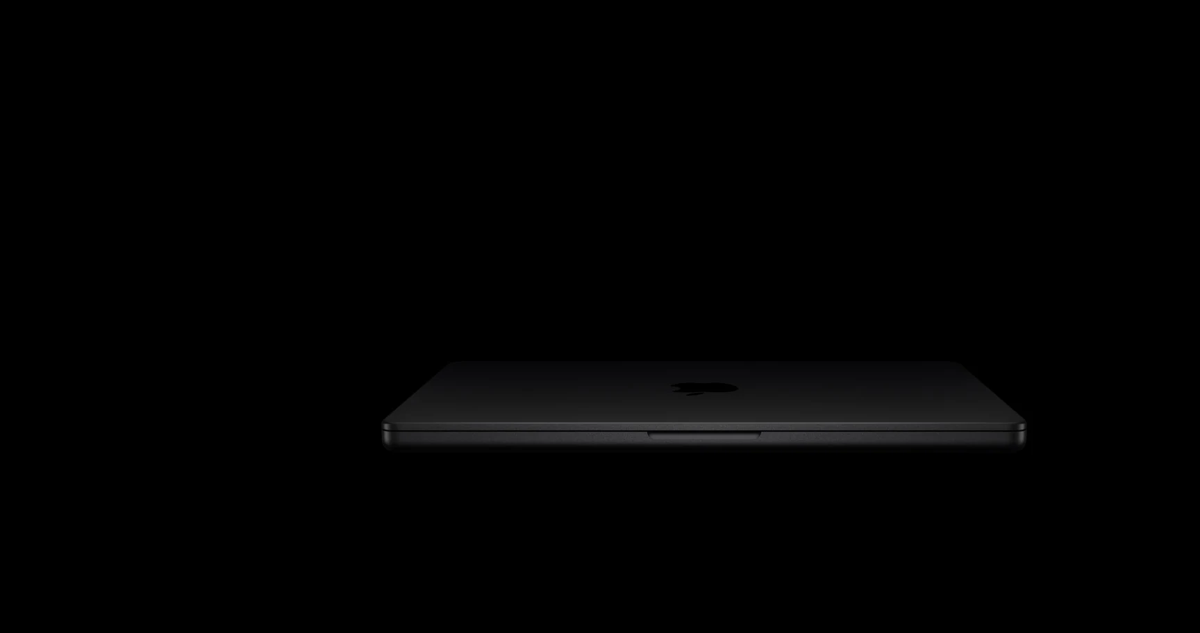 A dark-colored MacBook Pro is photographed from behind, showcasing its sleek design and the Apple logo on the back.