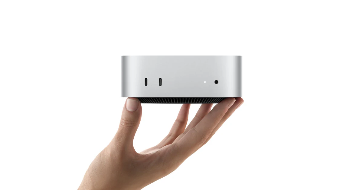 A hand holding a silver, rectangular device with ventilation grilles and small ports on the back.