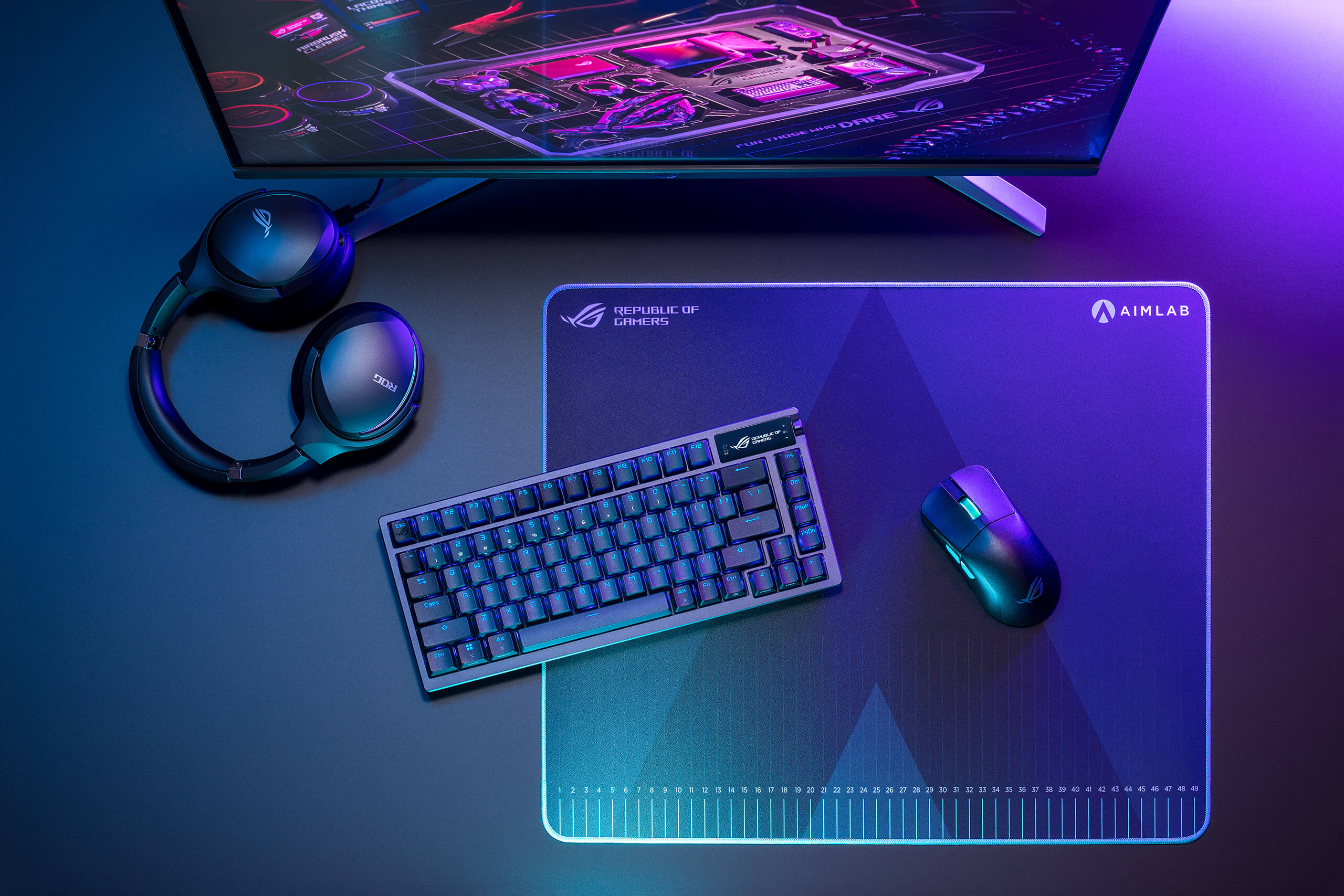 A top-down view of a gaming setup featuring a keyboard with RGB lighting, a mouse, headphones, and a mousepad with the Aimlab logo.