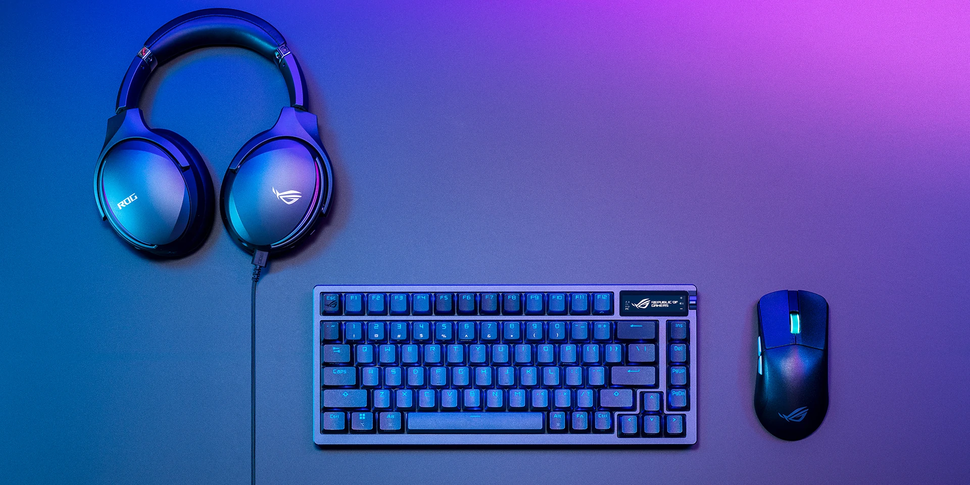 A top-down view of a blue ROG gaming headset with a coiled cable, a mechanical keyboard with RGB backlighting, and a black ROG gaming mouse on a gradient background.