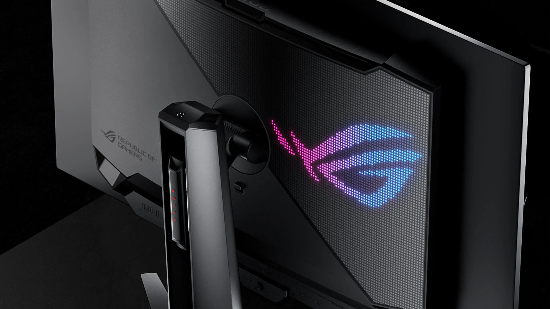 A close-up side profile of a black monitor with the ROG logo illuminated in pink and blue, featuring textured edges and a sleek design.
