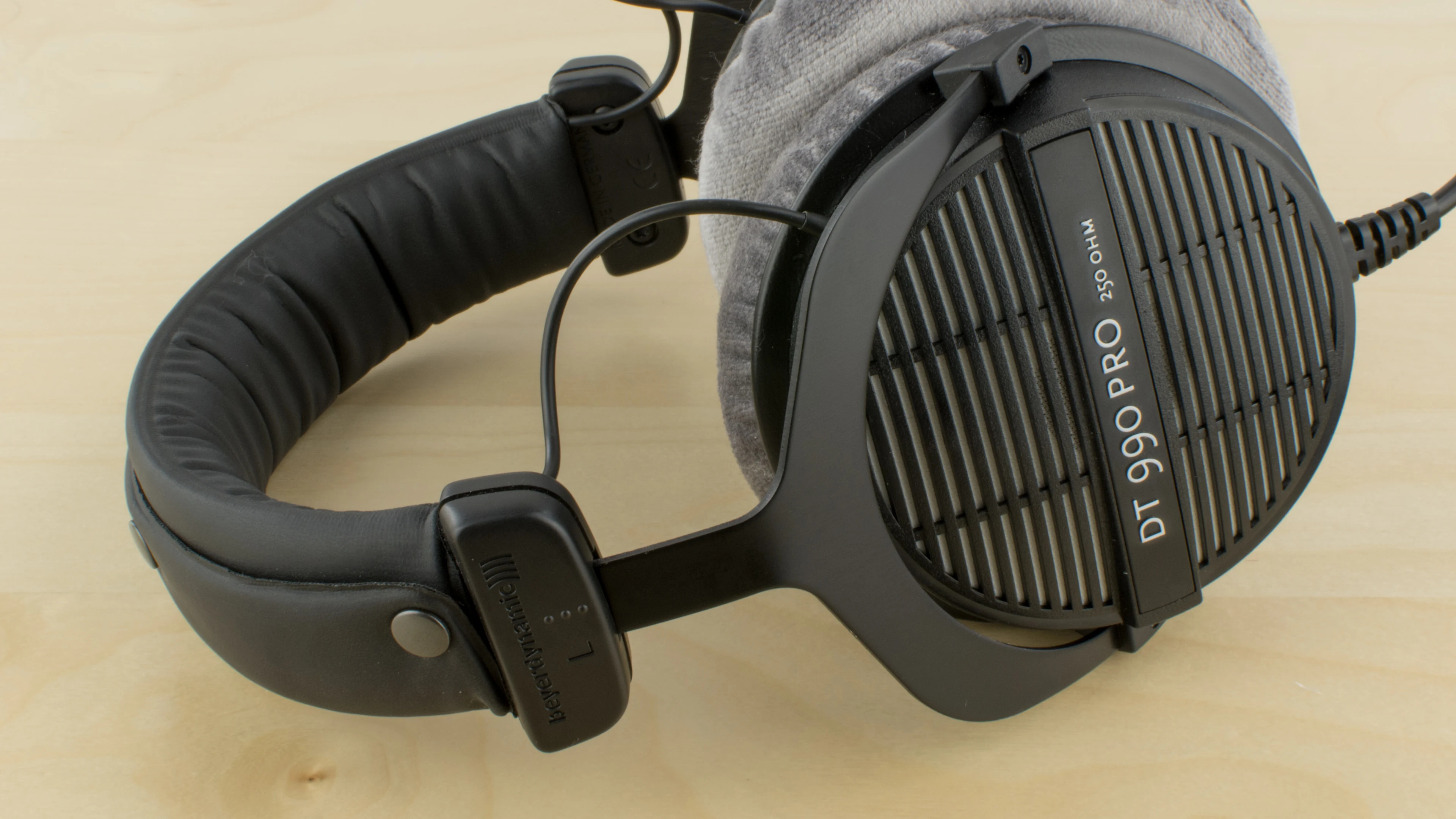 The Beyerdynamic DT 990 PRO is shown in a side profile, resting on a wooden surface with visible ear cups and headband.