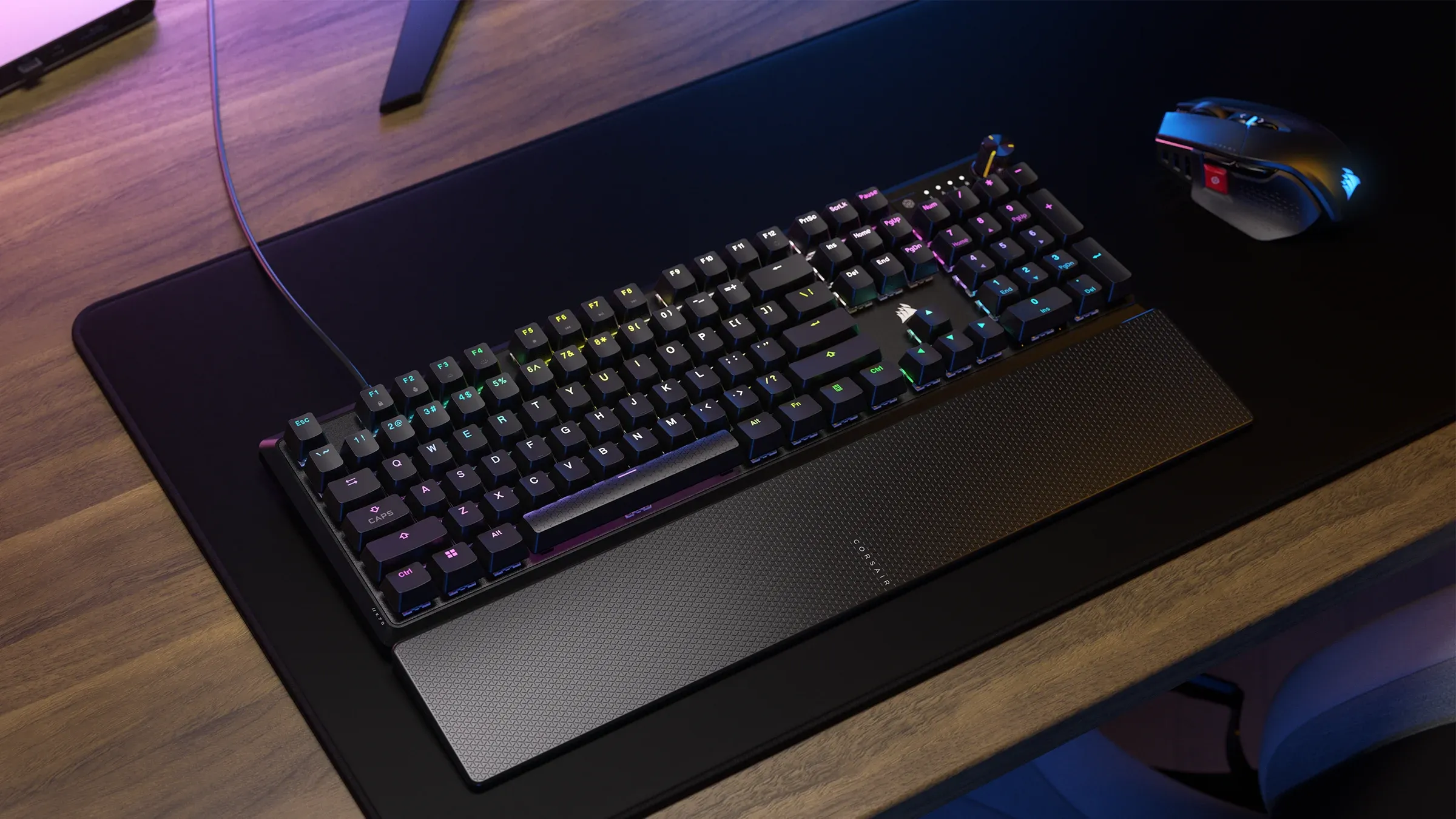 A Corsair K70 CORE RGB keyboard is shown in a top-down view on a desk with a mouse and wrist rest.