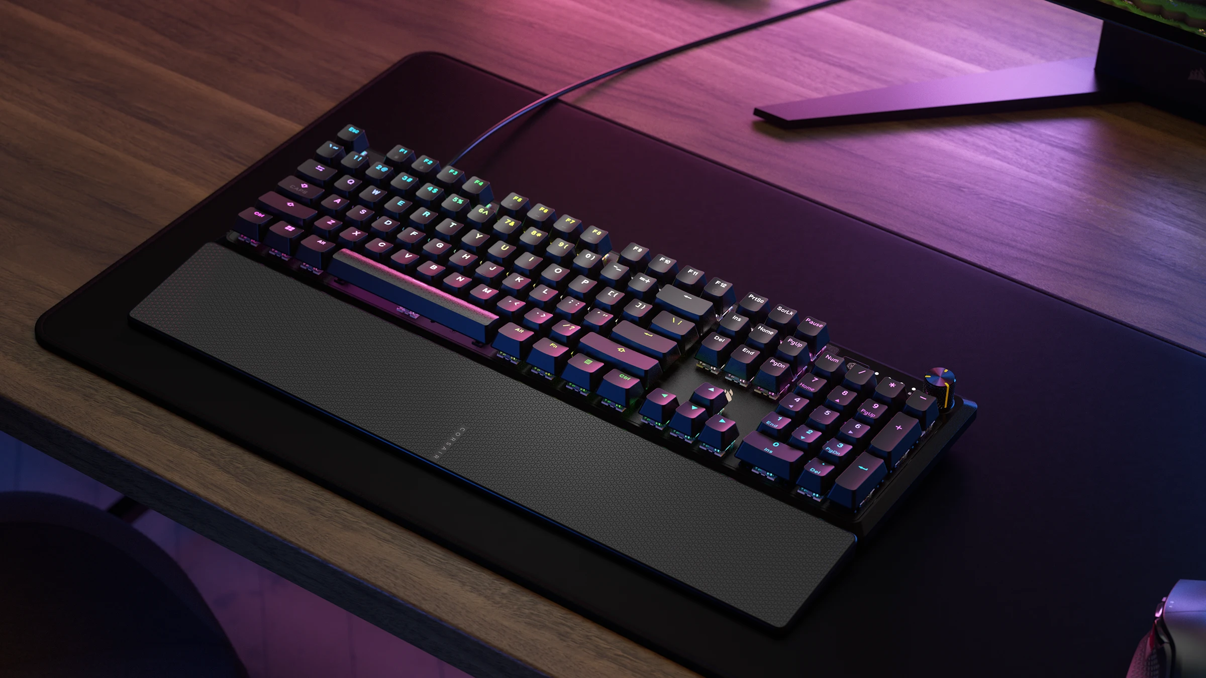 The keyboard is shown from a top-down angle on a desk, with a black wrist rest and a cable extending to the side.