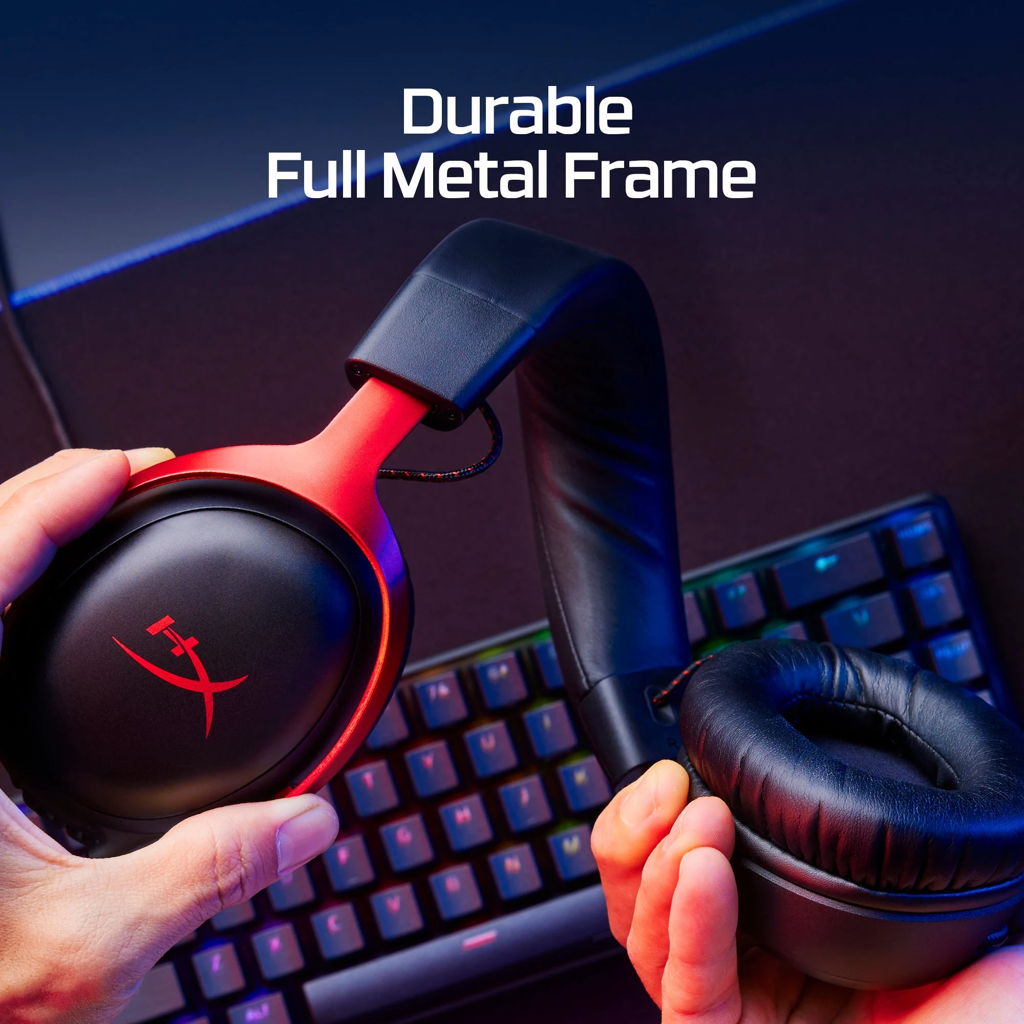 A close-up of a red HyperX Cloud III headset with a durable full metal frame, held in hands against the backdrop of a gaming setup.
