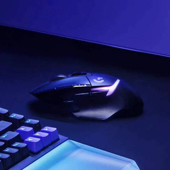 The Logitech G502 X Plus mouse is shown in a side profile, resting on a desk with a keyboard partially visible in the foreground.