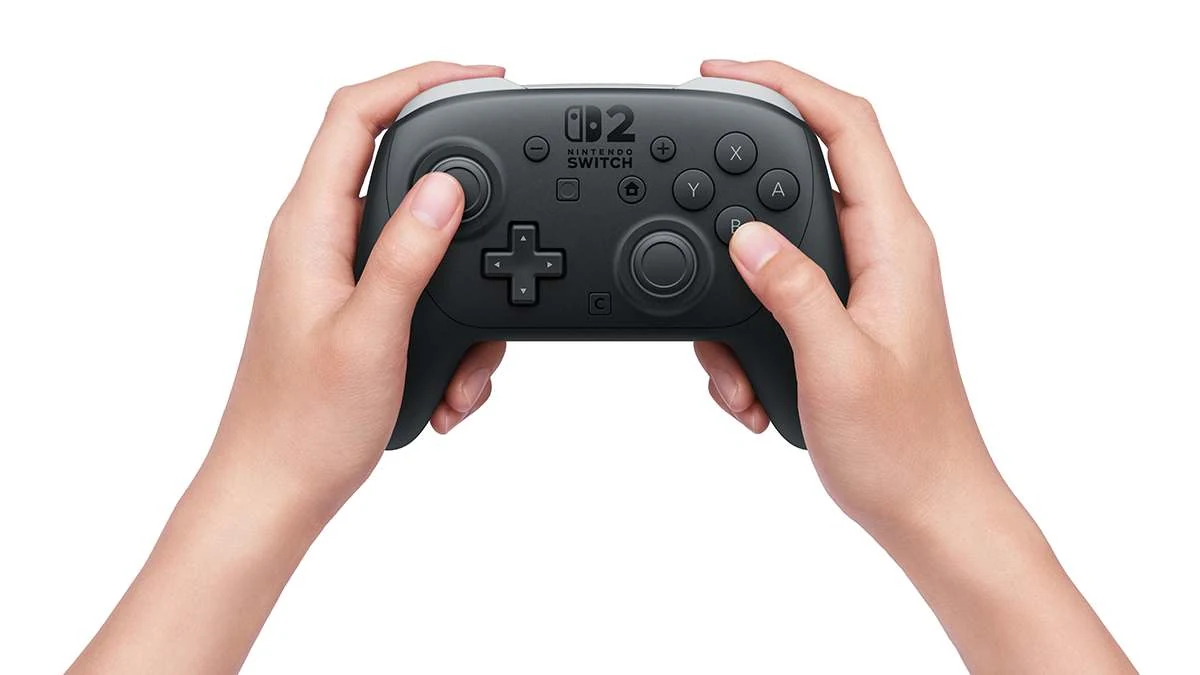 A black Nintendo Switch Pro Controller held in hands, showing the top view with visible buttons and joysticks.