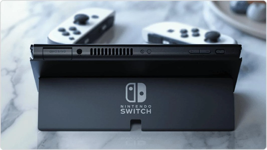 The Nintendo Switch OLED Model with White Joy-Con Controllers is shown from a top-down perspective, highlighting its black color and the Nintendo logo on the back.