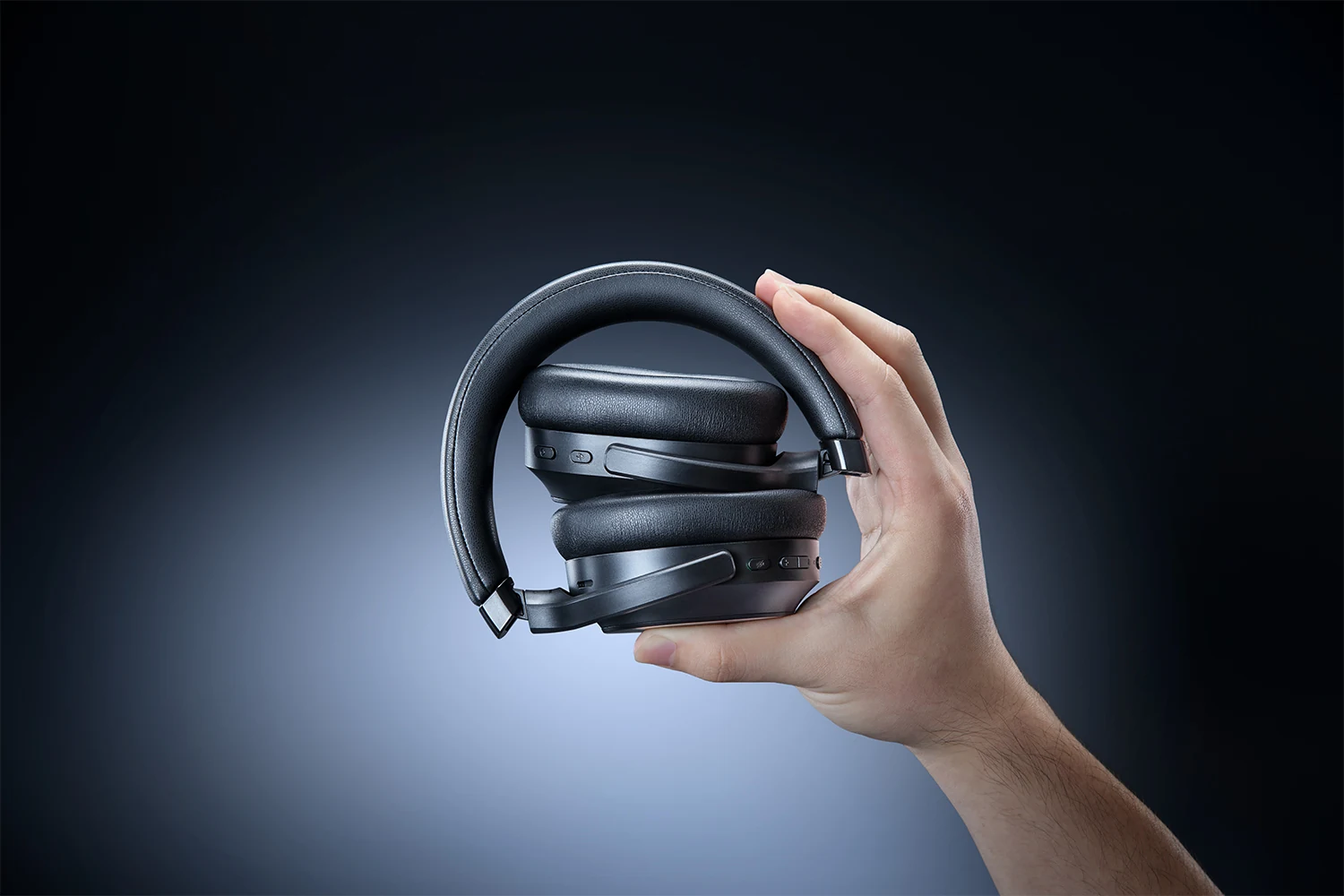 A hand holding a black over-ear headset with visible buttons and a cable.