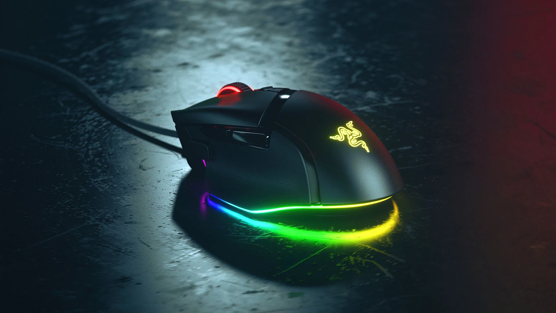 A black gaming mouse with a glowing Razer logo on top is shown in a three-quarter view, resting on a dark textured surface illuminated by colorful ambient lighting.