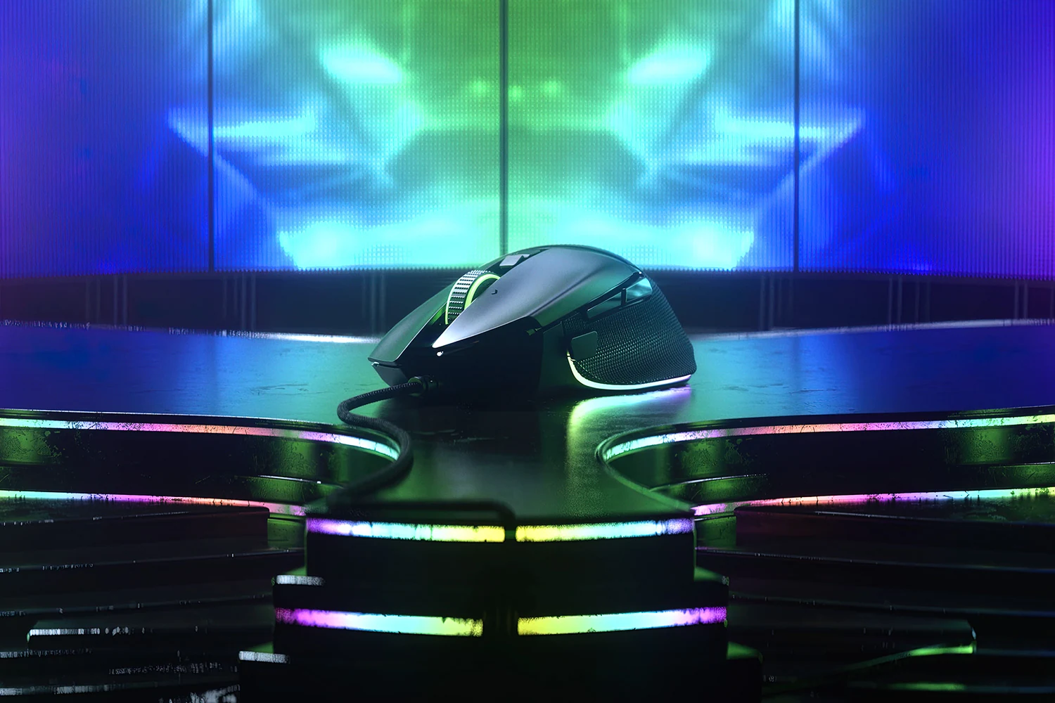 A black gaming mouse with a glossy finish is placed on a reflective surface with colorful LED lighting in the background.