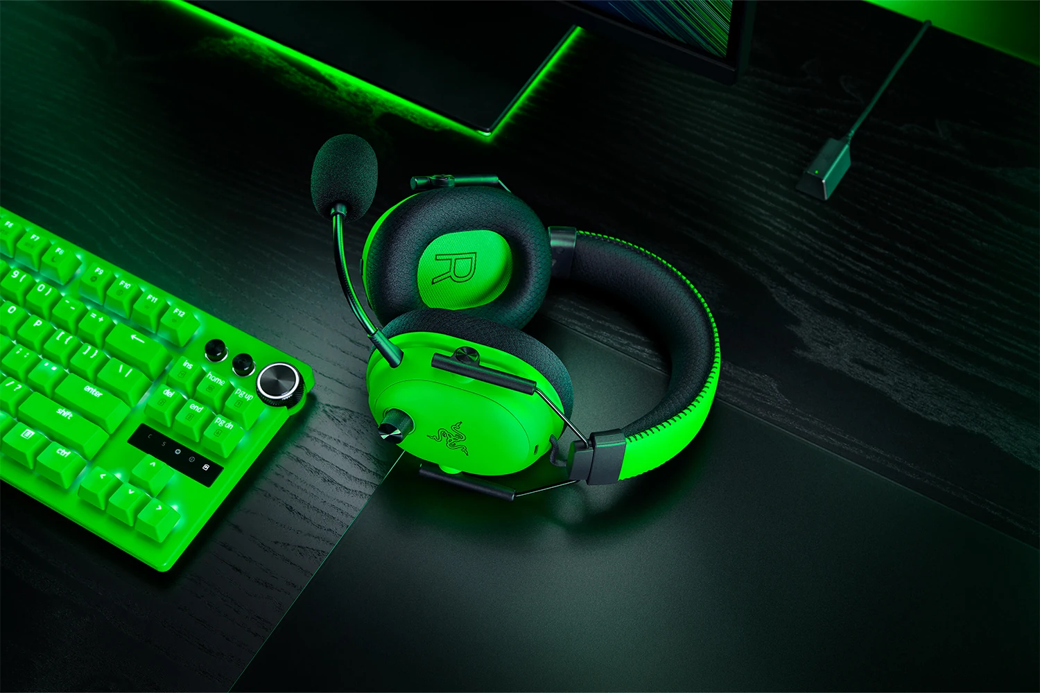 A green and black Razer BlackShark V3 Pro Esports Green Edition headset with a microphone is shown resting on a desk next to a matching green keyboard.