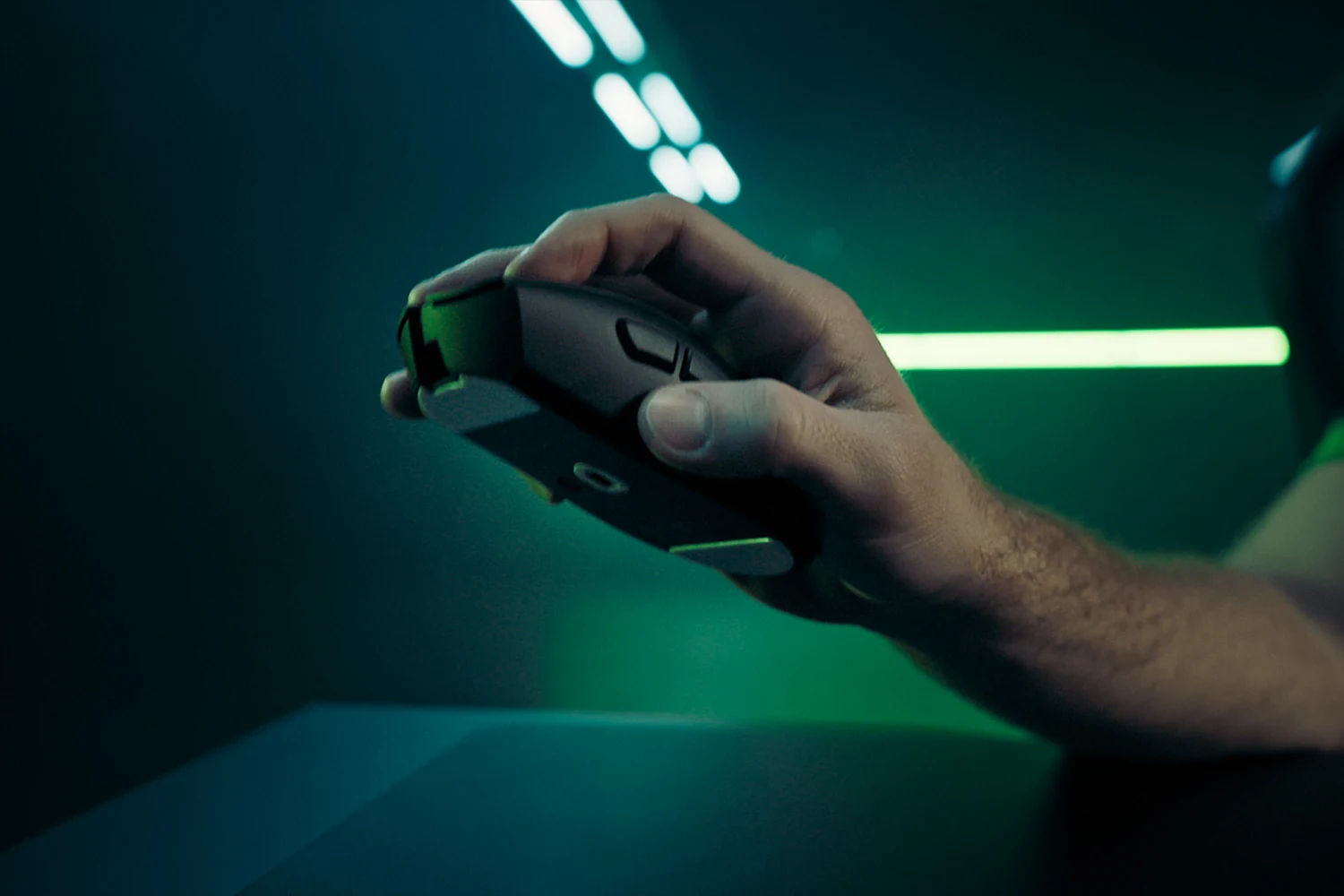 A hand holding a black and green gaming mouse with textured grip, taken from an in-hand perspective.