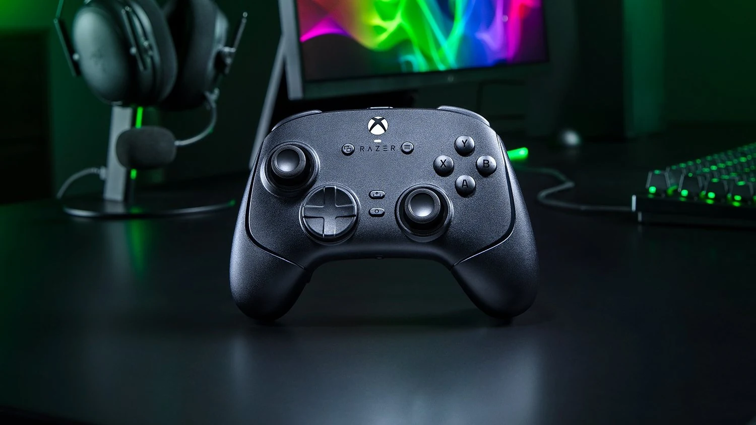 A black Razer Wolverine V4 Pro controller is shown in a three-quarter angle on a dark desk, with a headset and keyboard visible in the background.