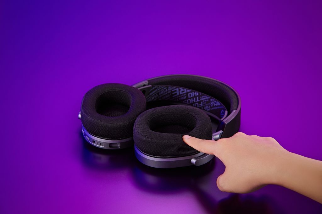 A close-up of a black gaming headset with a hand pointing at the ear cup.