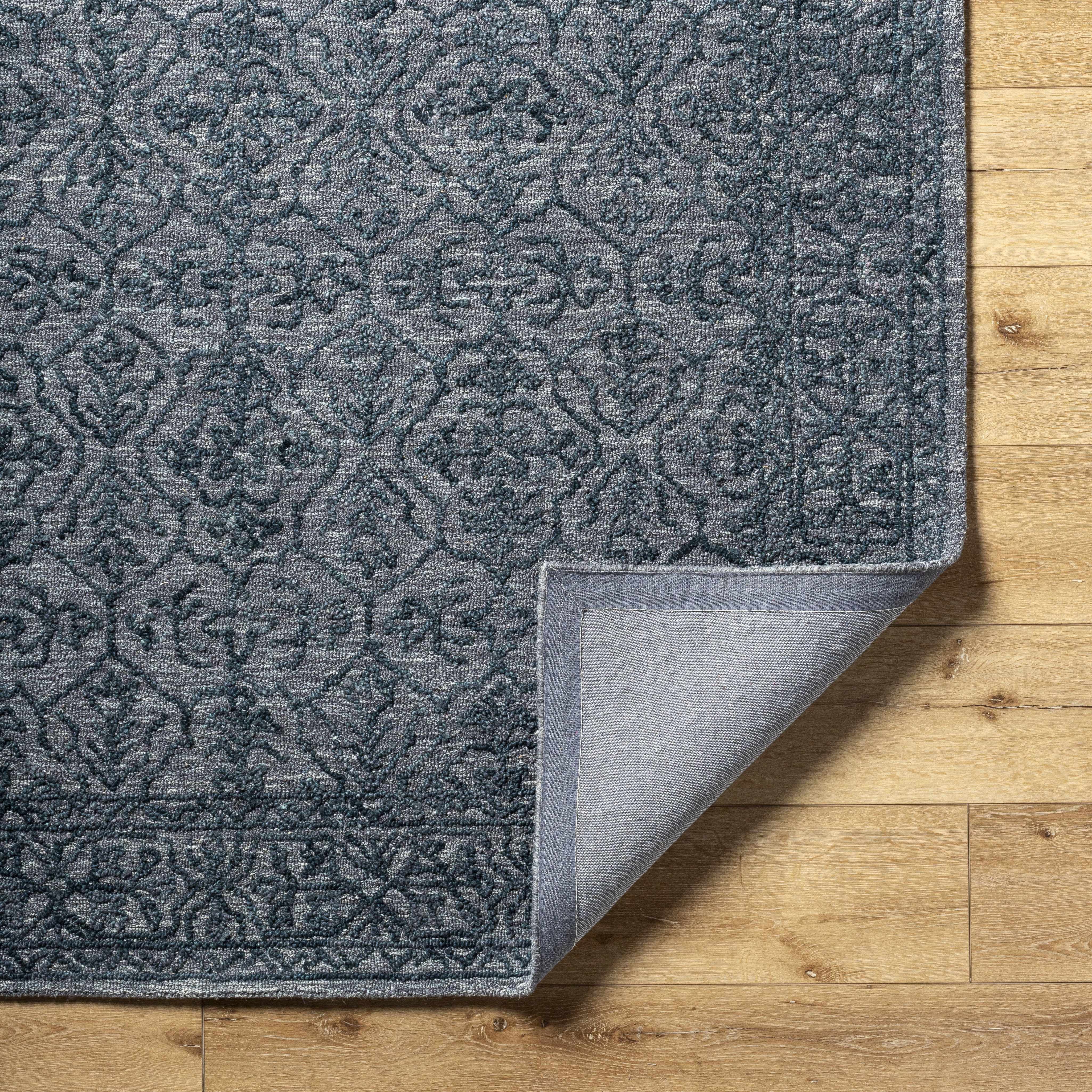 A close-up view of a dark blue area rug with intricate patterns, placed on a wooden floor.
