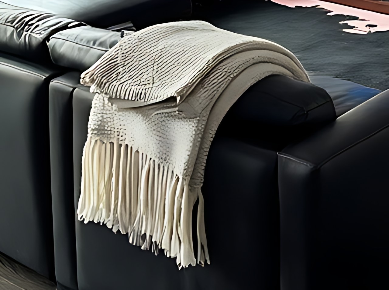 Close-up of an ivory chenille throw blanket draped over a black leather sofa.