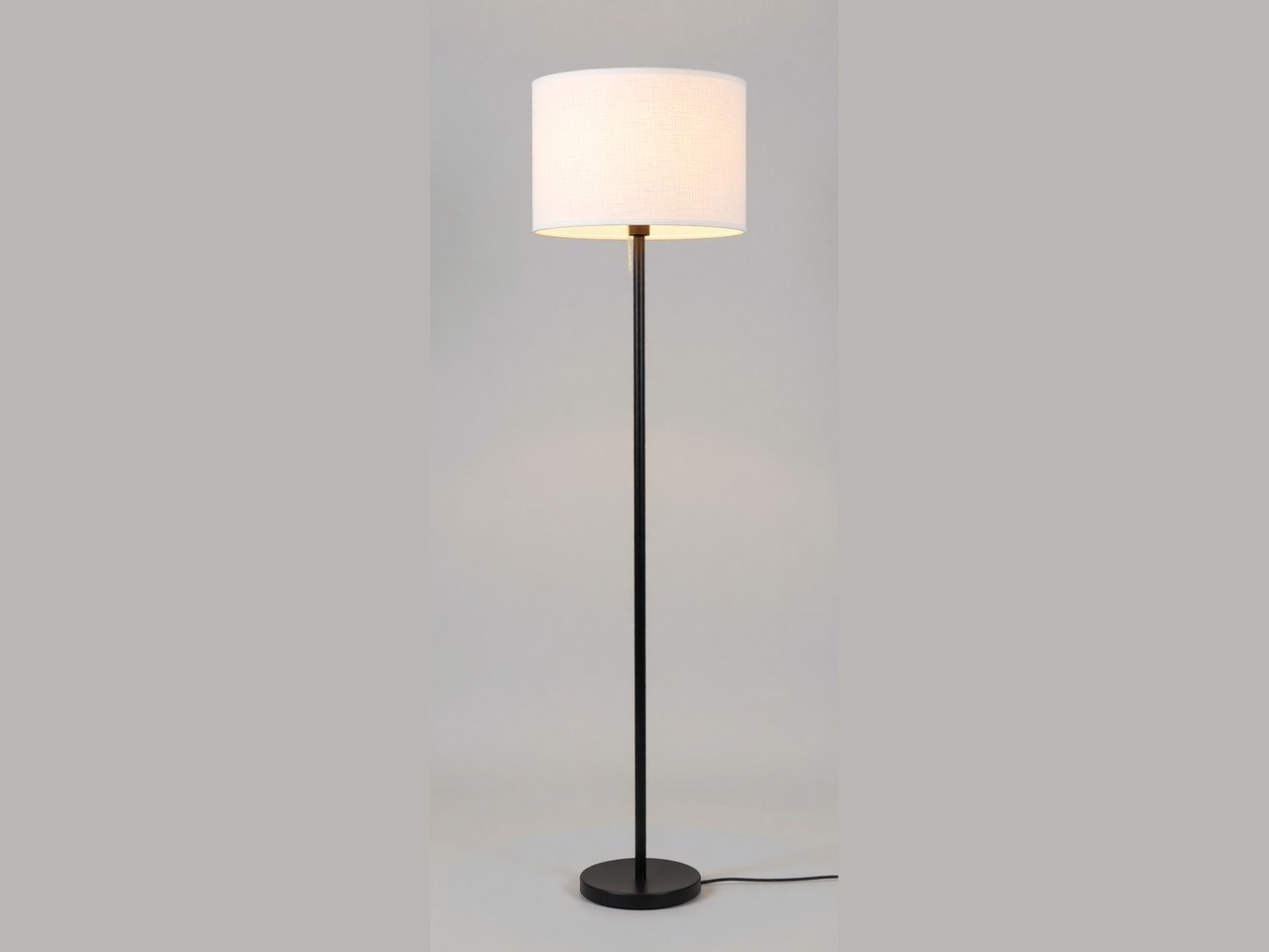 A black pole floor lamp with a white linen drum shade, shown on a plain grey background.