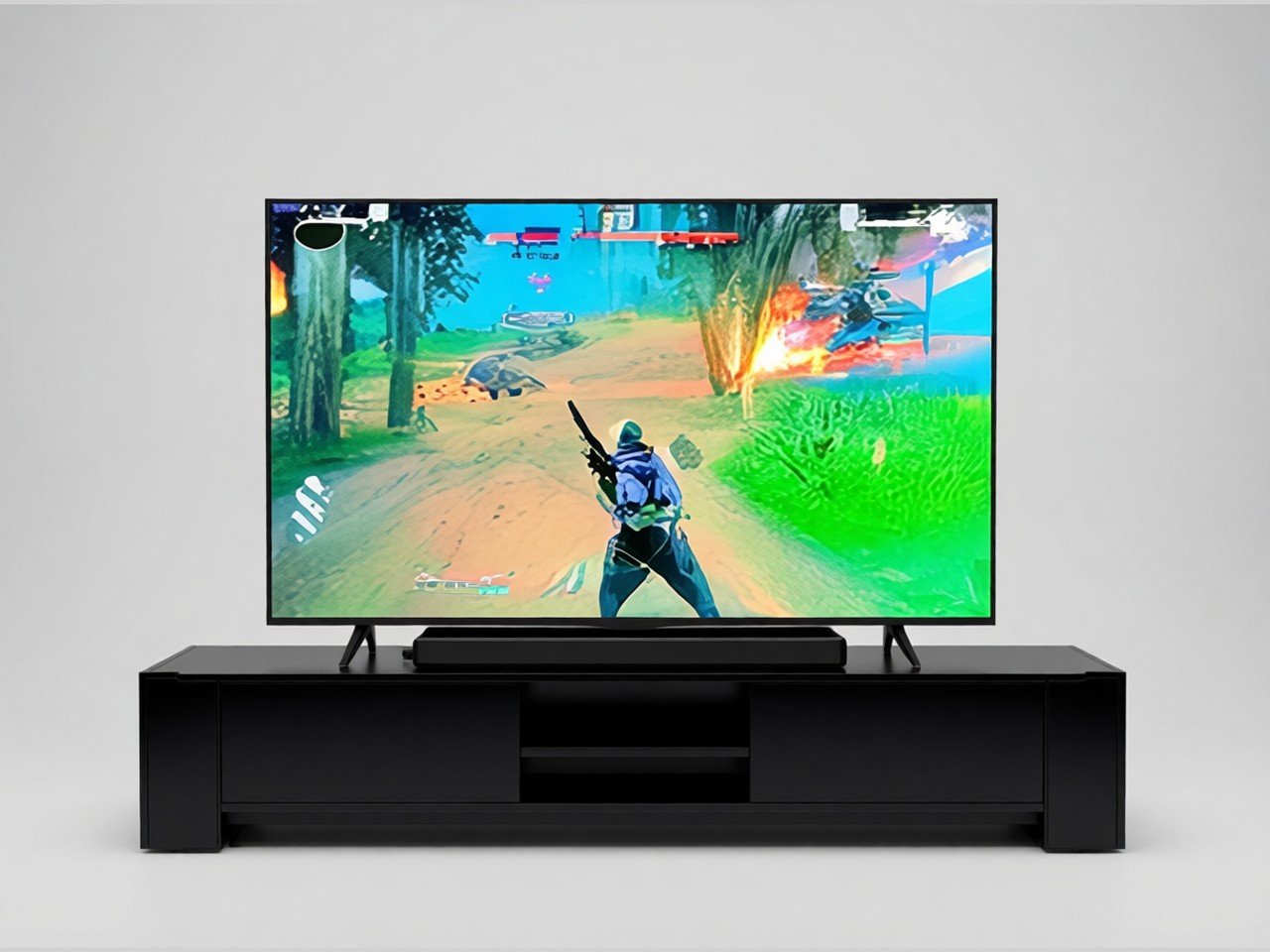 A large flat-screen TV on a black media console showing a colorful action game, on a plain grey background.