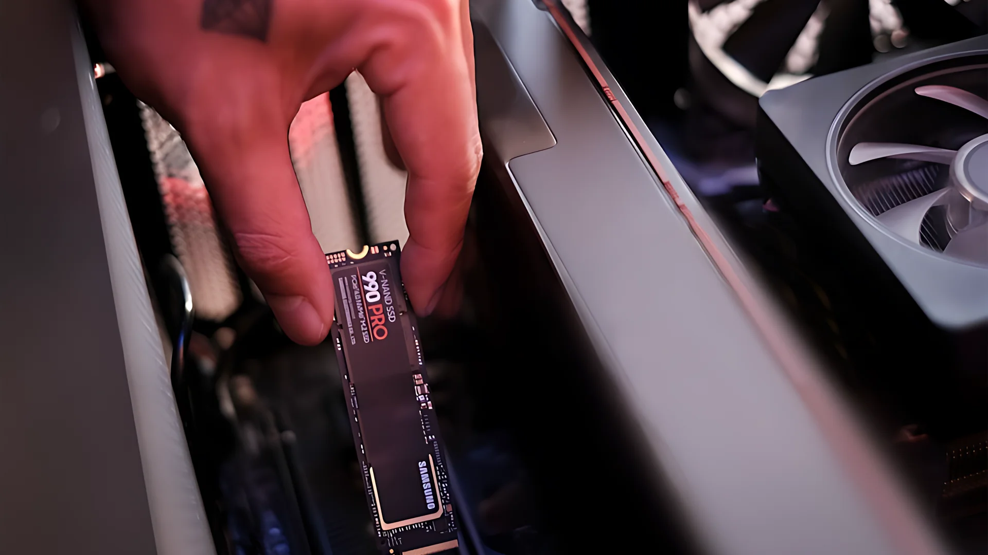 A hand holding a Samsung 990 PRO SSD in front of an open computer case.